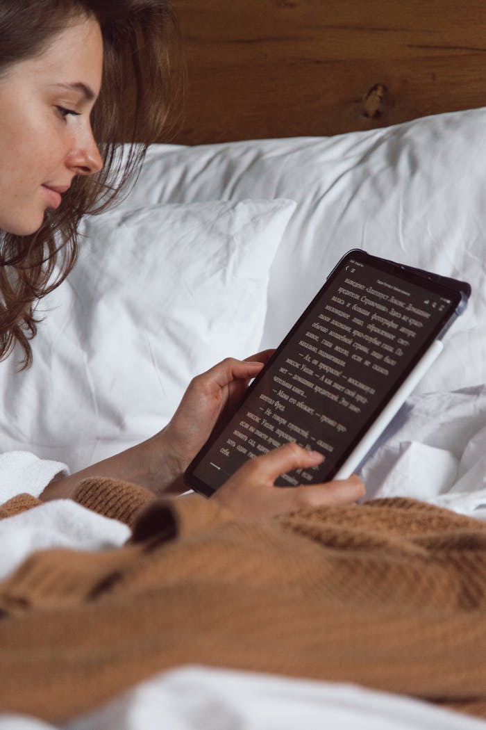 A woman reading on her tablet while lying in bed, creating a cozy and relaxed atmosphere.